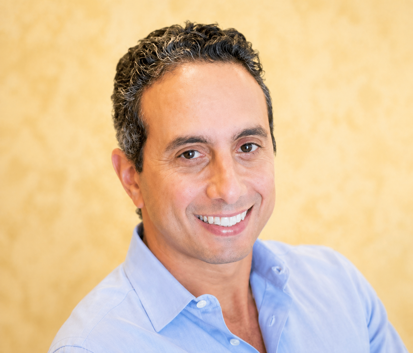 A person smiling in a light blue shirt against a yellow background.
